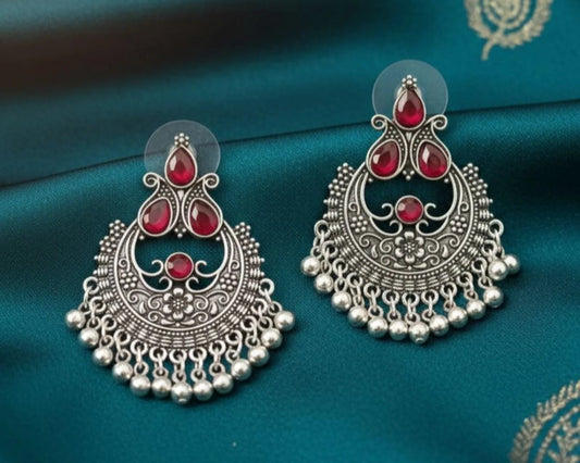 Ornate silver earrings with red stones on a blue fabric background