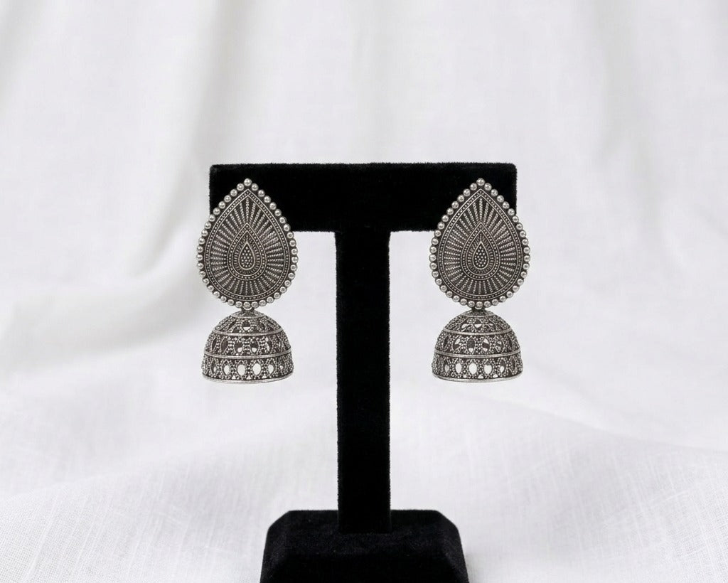 Pair of silver earrings on a black stand against a white background