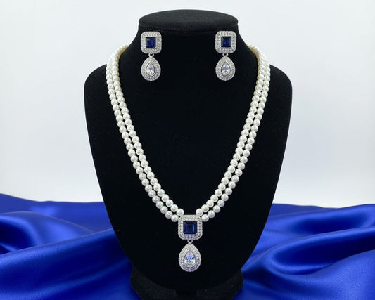 Pearl necklace with diamond pendants on a black stand against a blue fabric background
