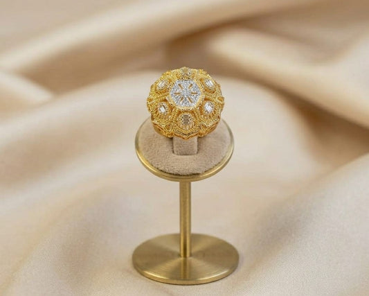 Gold ring with intricate design on a matching stand against a beige fabric background