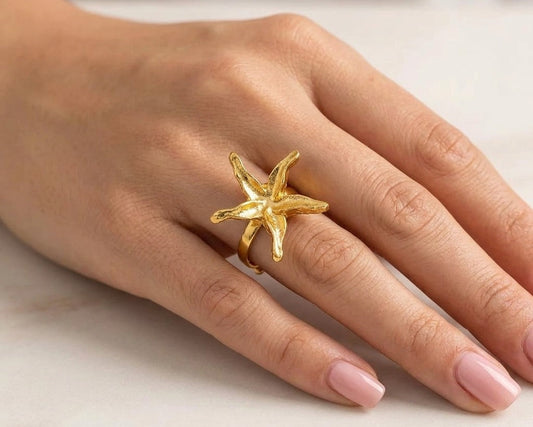 Gold starfish ring on a person's finger against a neutral background