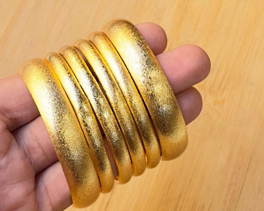 Gold bangles held in a hand on a wooden surface