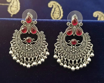 Ornate silver earrings with red stones on a blue fabric background