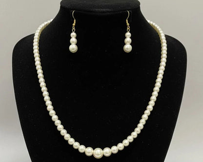 Pearl necklace and earrings set on a black bust against a white background