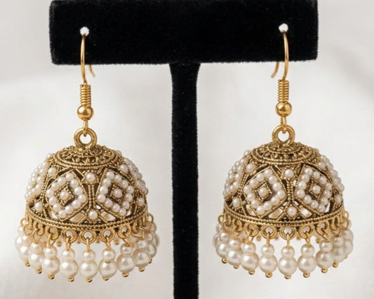 Pair of gold and pearl earrings on a black stand against a white background