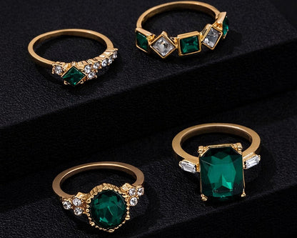 Four gold rings with green gemstones on a black background