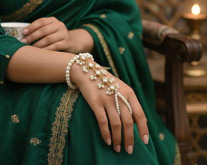 Person wearing a green saree with gold embroidery, holding a cup, and wearing a pearl bracelet.