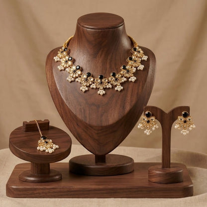 Gold-toned traditional Indian jewelry set including a statement necklace, earrings, and a maang tikka, displayed on a wooden jewelry stand set against a beige fabric backdrop.
