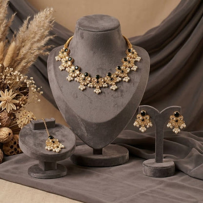 Gold and white floral jewelry set displayed on gray velvet stands, including a necklace, earrings, and a matching pendant, styled with dried pampas grass and neutral fabric in the background.