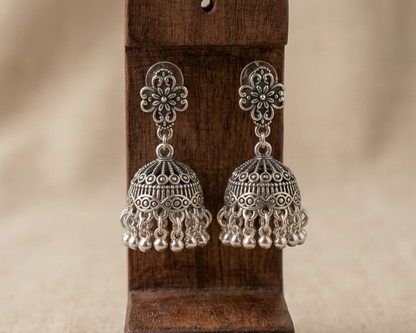 Pair of silver earrings on a wooden stand with a beige background
