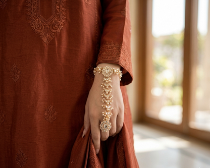 Person wearing a rust-colored embroidered outfit with jewelry, standing indoors.