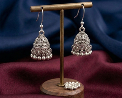 Silver jhumka earrings on a wooden stand with a blue and red fabric background
