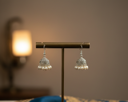 Pair of silver earrings on a gold stand with a blue fabric background