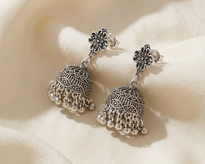 Pair of silver earrings on a soft beige fabric background