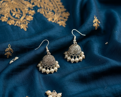 Silver earrings with pearls on a blue fabric background