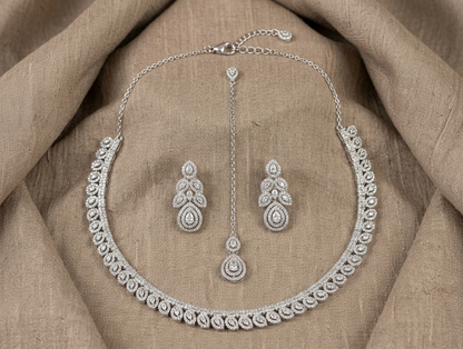 Silver necklace and earrings set on a beige fabric background