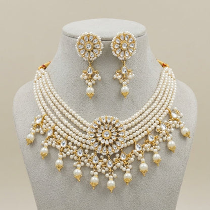 A traditional Indian jewelry set featuring a multi-strand pearl necklace with gold-plated embellishments, a matching round stud earring, and a central floral pendant, all displayed on a gray velvet jewelry bust against a light beige background.