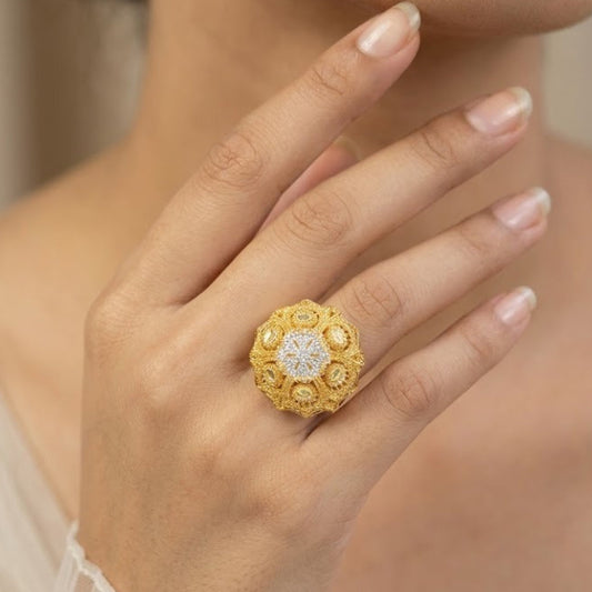 A close-up of a woman's hand wearing a large, ornate yellow gold ring with a floral, textured halo design and a clear central gemstone.