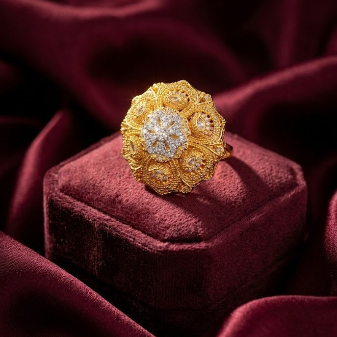 A gold ring with a floral, textured pavé center and clear stones, displayed on a deep burgundy velvet ring box against a matching draped velvet background.