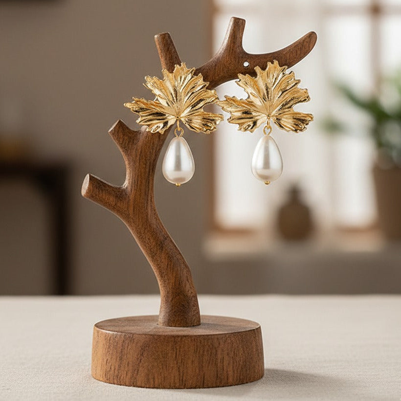 Gold earrings with pearl drops on a wooden stand against a blurred indoor background