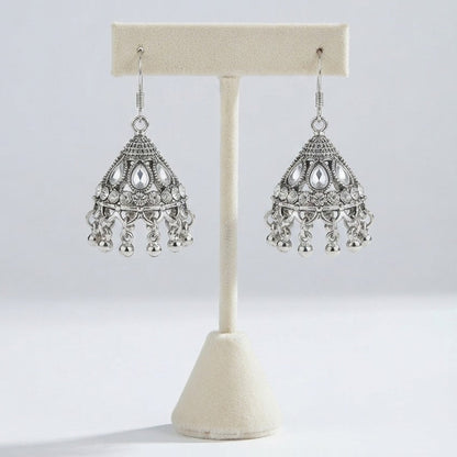 A pair of silver-toned traditional Indian jhumka earrings displayed on a cream-colored jewelry stand against a light gray background.