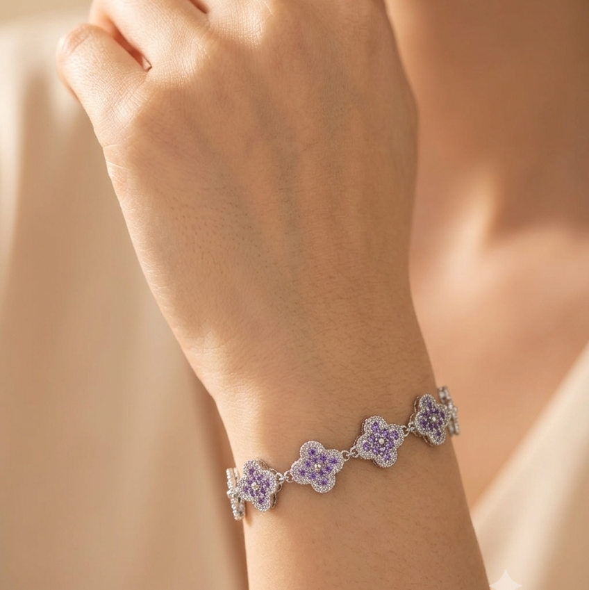 A close-up of a model's wrist wearing a delicate silver-toned bracelet with five floral clusters, each set with light purple stones and small clear accent stones.