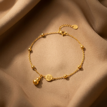 A delicate gold chain bracelet with small bead accents and a small hanging charm, displayed on draped beige satin fabric.