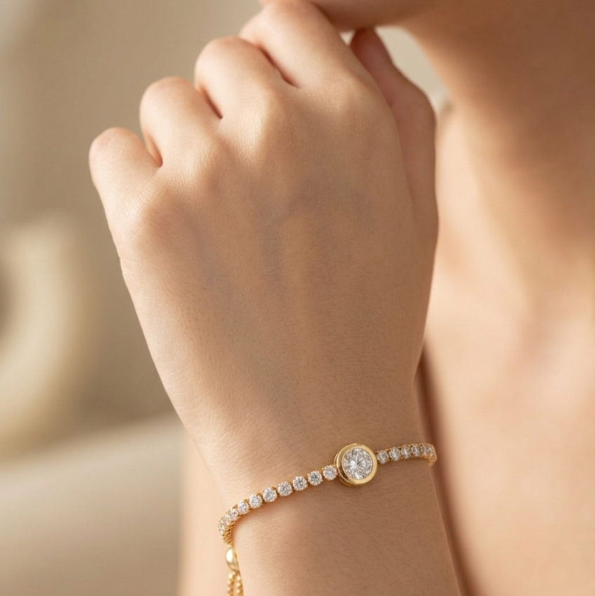 A close-up lifestyle shot of a delicate gold bracelet with a central round crystal and a dangling chain, worn on a woman's wrist.