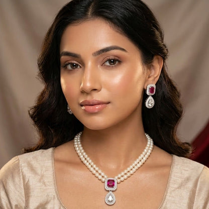 A woman wearing a matching pearl necklace and drop earrings with square pink gemstones and silver settings, shown in a close-up portrait against a draped beige background.