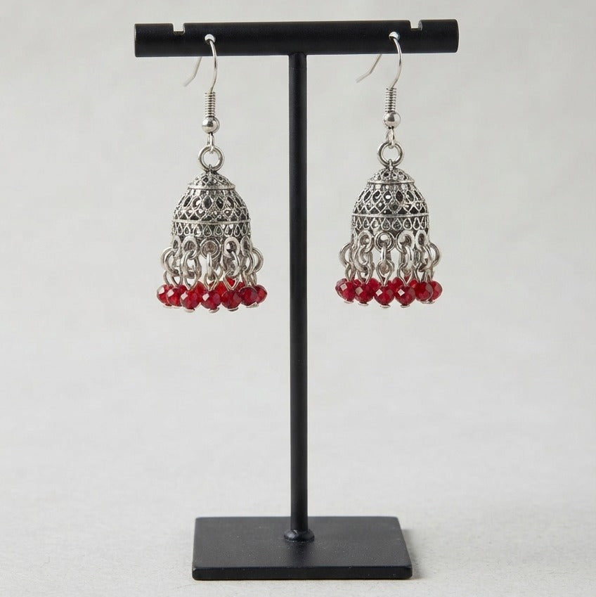 Silver-toned filigree dangle earrings with small red bead drops, displayed on a black stand against a light gray background.