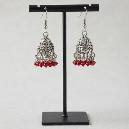 Silver-toned filigree dangle earrings with small red bead drops, displayed on a black stand against a light gray background.