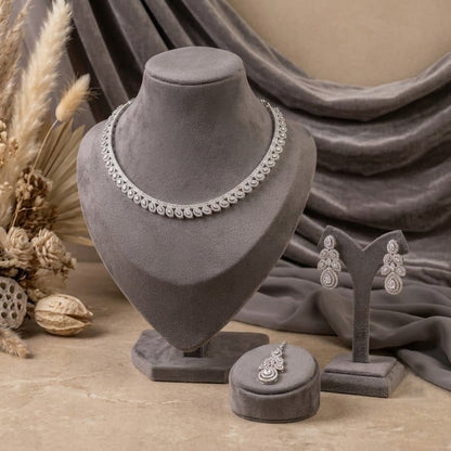 Silver-toned jewelry set displayed on gray velvet stands, including a necklace, earrings, and ring, arranged with dried botanical decor and draped fabric in a styled studio setting.