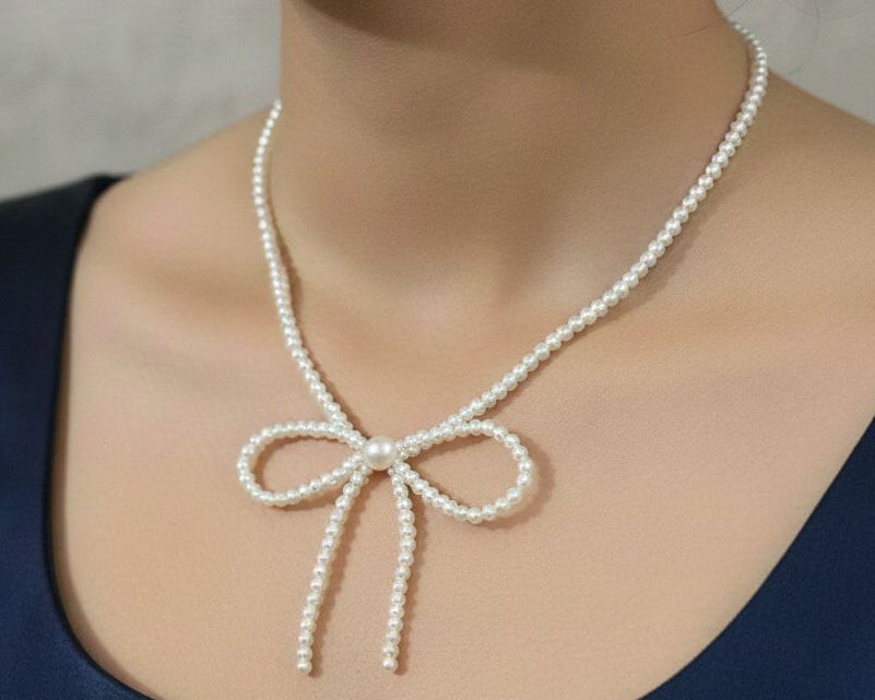 Pearl necklace with a bow detail worn by a person against a neutral background