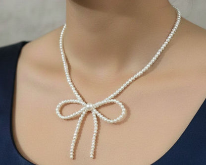 Pearl necklace with a bow detail worn by a person against a neutral background