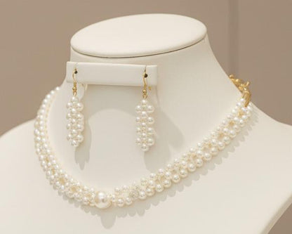 Pearl necklace and earrings set on a mannequin bust against a beige background