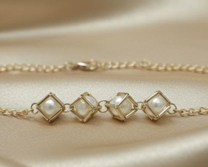 Gold bracelet with diamond-shaped pendants on a beige fabric background