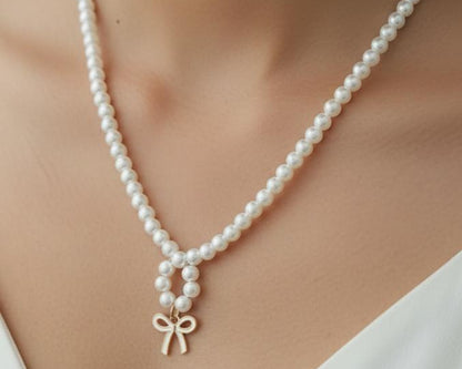 Pearl necklace with a gold bow pendant on a person wearing a white top.