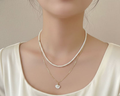 Pearl necklace and gold pendant on a person wearing a white satin top.