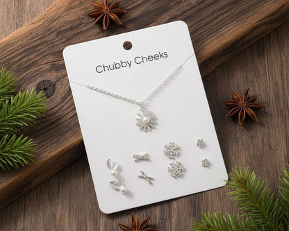 Silver jewelry set on a 'Chubby Cheeks' branded card with Christmas decorations on a wooden surface.