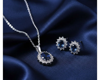 Silver jewelry set with blue gemstones on a dark blue fabric background