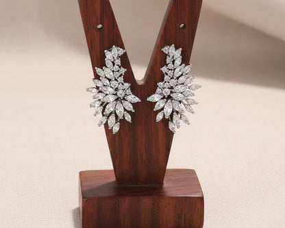 Pair of diamond earrings on a wooden 'Y' stand against a beige background
