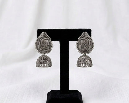 Pair of silver earrings on a black stand against a white background