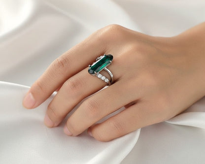 Hand wearing a ring with a green gemstone on a white fabric background