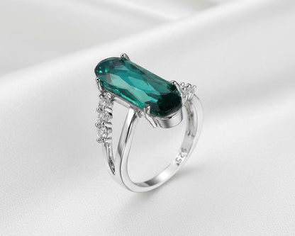 Silver ring with a green gemstone on a white satin background