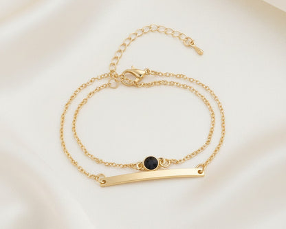 Gold bracelet with a black bead on a light beige background
