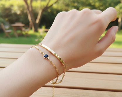 Hand wearing gold bracelets with a blurred garden background