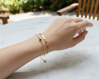 Hand wearing gold bracelets on a marble surface with a blurred outdoor background
