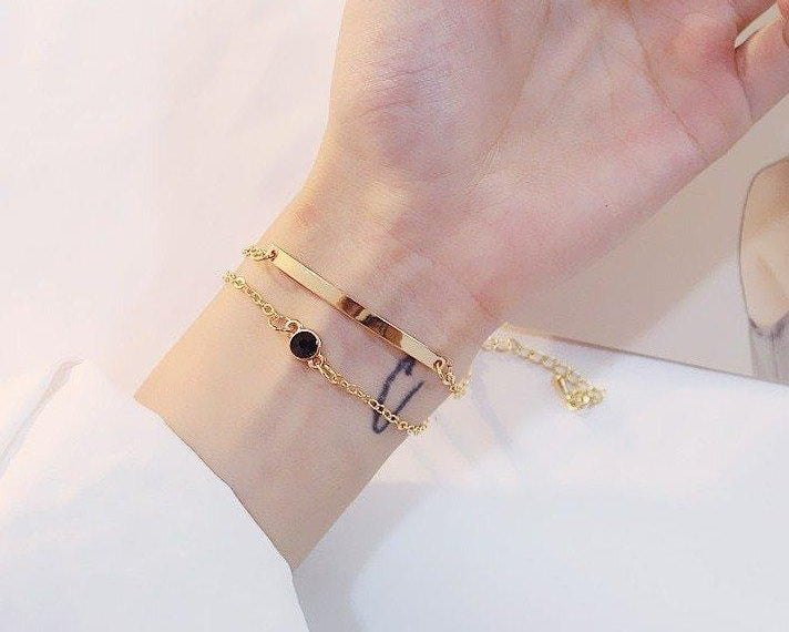 Gold bracelet with a small black gemstone on a wrist against a white background