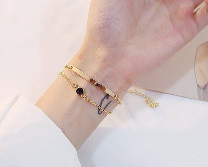 Gold bracelet with a small black gemstone on a wrist against a white background
