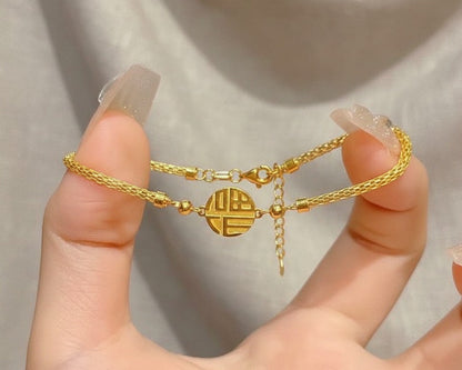 Gold bracelet with a circular charm held by a hand against a neutral background